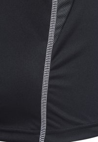 Zwarte sportstof met contrasterende witte stiksels. Heeft een textuur van gaas aan de zijkant voor ademend vermogen.