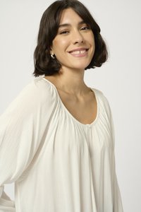 Lichte, crèmekleurige blouse van een gestructureerde stof, met een losse pasvorm en een ronde halslijn met zachte plooien en een enkele knoopdetail.