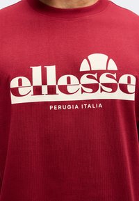 Κόκκινο φούτερ με μεγάλο λευκό λογότυπο "ellesse" και κείμενο "Perugia Italia" από κάτω στο στήθος.