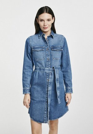 Jeansowa sukienka koszulowa z długimi rękawami, kieszeniami z przodu i paskiem w talii. Jasnoniebieski kolor, fason zapinany na guziki oraz zaokrąglony dół.