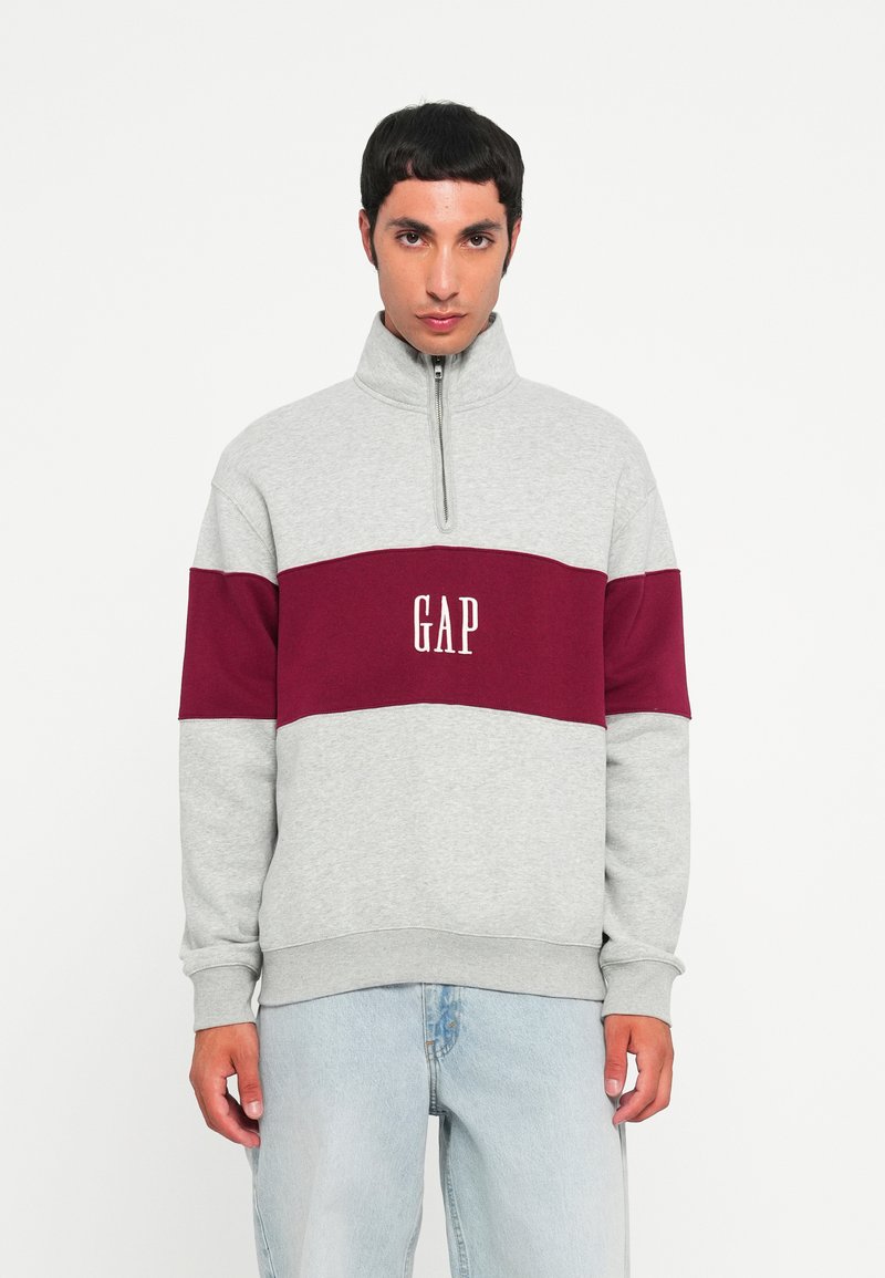Gray sweatshirt with a maroon horizontal band, featuring a quarter zip and "GAP" logo in white. Soft fabric, relaxed fit.