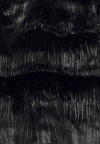 Svart faux päls tyg med varierande längder, med en glansig, texturerad yta och täta fibrer som skapar en lagerliknande look.