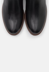 Bottines en cuir noir avec une finition lisse, bout rond et piqûres contrastantes le long de la semelle. Talon plat, design minimaliste.