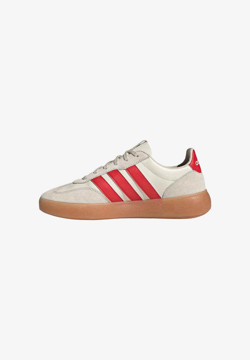 Zapatilla deportiva color crema con suela de goma, tres rayas rojas de Adidas en el lateral y lengüeta trasera roja con el logo blanco de Adidas.