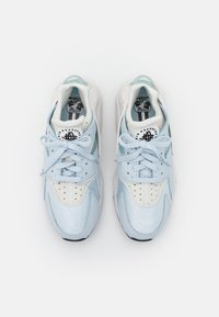Paire de baskets Nike bleu clair et blanc avec lacets, swoosh noir et logo « Air Huarache » sur la languette, vue de dessus sur fond blanc.