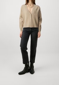 Beige ribbad cardigan med V-ringning, framfickor och fyra knappar, kombinerad med mörk denimjeans och svarta ankelboots. Mjuk textur.