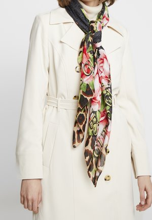 Trench-coat blanc ceinturé porté sur un col roulé, associé à une écharpe colorée à imprimé floral et léopard nouée au cou.