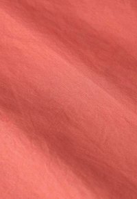 Korallfarbener Baumwollstoff mit einer subtilen Textur, der eine weiche, glatte Oberfläche und sanft geschwungene Falten zeigt. Keine Muster oder Akzente sind sichtbar.
