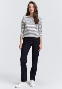 Rutet langermet skjorte, hvit og marineblå, sammen med mørkeblå jeans med oransje sømmer og hvite joggesko, stående på en lys bakgrunn.