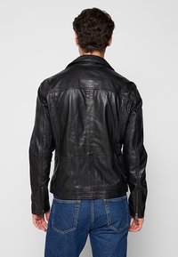 Veste en cuir noire avec un col classique, un design ajusté, des coutures tailleur et des poignets zippés, assortie à un jean en denim bleu.