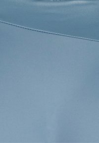 Tecido azul claro com uma textura suave e mate, e uma cintura que apresenta um detalhe de costura discreto. O material parece ser elástico e respirável.