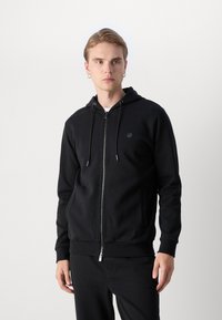 Felpa nera con zip e cappuccio regolabile, slim fit, realizzata in tessuto morbido. Presenta un patch del logo sul petto e polsini a costine.