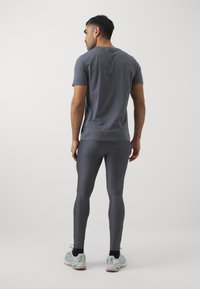 Szürke sportpóló rövid ujjakkal, hozzá illő szürke leggings-szel párosítva. Simaságot és testhezálló fazont kínál. Ezüst futócipők.