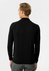 Zwarte lange mouw trui met een geribbelde kraag en textuur breiwerk. Heeft een getailleerde silhoët en minimale naden, wat zorgt voor een strakke afwerking.