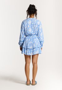 Robe à motif floral bleu avec jupe à volants, manches longues et taille cintrée. Fabriquée dans un tissu léger, elle présente un design décontracté.