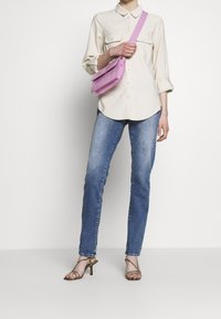 Camisa de botones color beige claro, pantalones vaqueros azules, bolso cruzado rosa con un acabado texturizado y sandalias marrones con tiras. Diseño sencillo, look casual.
