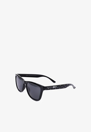 Black sunglasses with a cat-eye design, dark lenses, and a textured black-and-white dotted pattern on the temples, featuring the brand name.