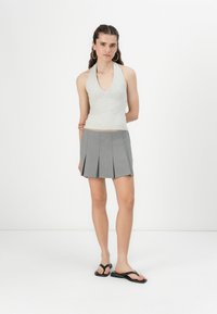Sivý halter top kombinovaný so sivou plisovanou mini sukňou a čiernymi šľapkami. Top má hlboký výstrih do V.