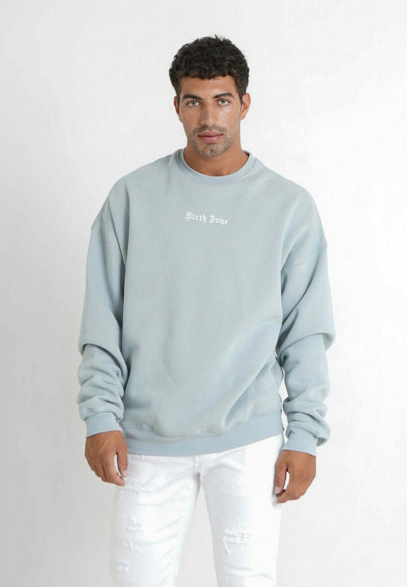 Sudadera azul claro hecha de un tejido suave, con un cuello redondo y un corte holgado. Texto blanco "Sixth June" en el pecho, combinada con unos jeans blancos desgastados.
