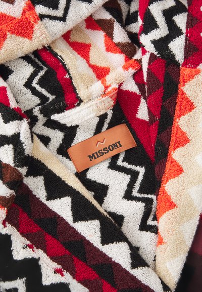 Tkanina s teksturom u cik-cak uzorku crvene, crne, bež i narančaste boje; oznaka glasi "MISSONI" na smešnom kožnom zakrpu.