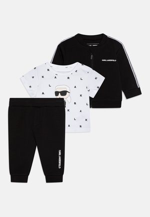 Ensemble pour enfants en trois pièces comprenant une veste noire zippée avec des rayures blanches, un T-shirt blanc avec un imprimé graphique et un pantalon noir.