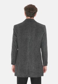 Cappotto grigio a spina di pesce con una vestibilità sartoriale, dotato di rever a punta, maniche lunghe e uno spacco sul retro. Realizzato in tessuto texturizzato.