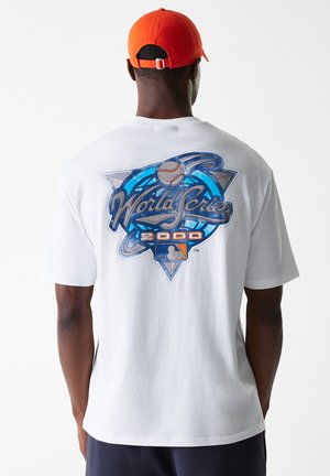 White cotton t-shirt featuring a colorful "World Series 2000" graphic on the back, with blue and gray accents. Wearer has an orange cap.