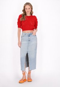Rød cropped strikket sweater med teksturerede hjerte-mønstre, parret med en høj talje denim nederdel med en forkantsslids, og orange platform sandaler.