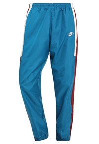 Blå Nike joggingbyxor med elastisk midja och fållar, som har vita och vinröda sidostråk och en vit Nike-logotyp på högra låret.