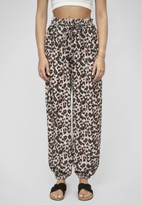 Pantalon en tissu léger avec un motif léopard, doté d'une taille élastique et de poignets froncés. Porté avec des sandales ouvertes noires.