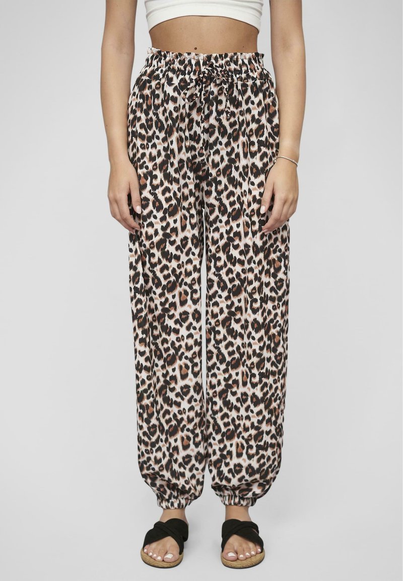 Pantalon en tissu léger avec un motif léopard, doté d'une taille élastique et de poignets froncés. Porté avec des sandales ouvertes noires.