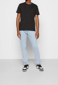 Camiseta de algodón negra con cuello redondo, combinada con jeans azul claro y zapatillas negras con detalles en blanco. Diseño simple, sin patrones.