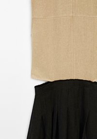Zweiteiliges Kleid mit einem beige strukturierten Oberteil und einem schwarzen, plissierten Rock. Das Oberteil hat einen geraden Schnitt, und der schwarze Stoff ist leicht ausgefranst.