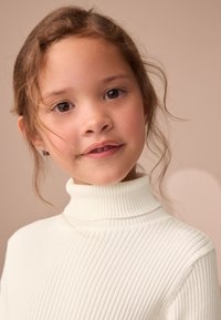 Pull à col roulé blanc côtelé avec un col haut. Texture lisse et coupe ajustée. Tissu doux, détails minimaux, adapté pour une tenue décontractée.