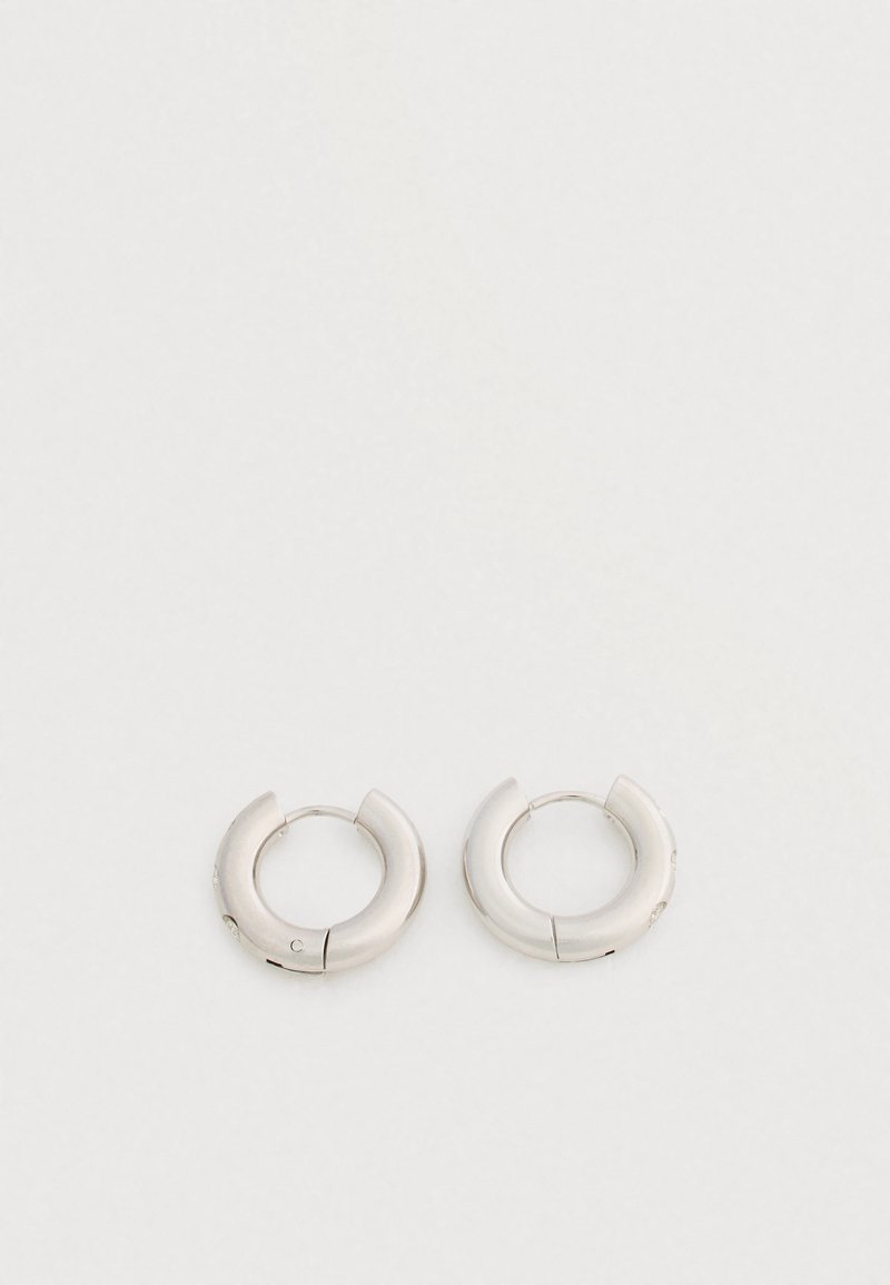 Ζευγάρι μικρών, χοντρών ασημένιων σκουλαρικιών κρίκων με λεία, γυαλιστερή επιφάνεια σε απλό λευκό φόντο.