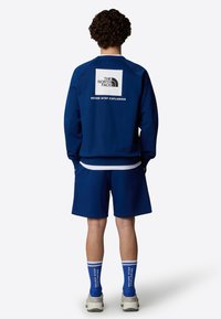 Granatowa bluza z białym logo na plecach, połączona z dopasowanymi szortami. Uzupełniona niebieskimi skarpetkami z napisem oraz szarymi trampkami.