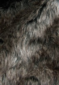 Tessuto in pelliccia finta nei toni grigio scuro e argento, caratterizzato da un pelo lungo e testurizzato con un aspetto morbido e soffice. Nessun motivo o elemento decorativo visibile.