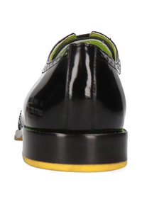Schwarzer Lacklederschuh mit abgerundeter Zehenpartie, grünem Futter, glatter Textur und einer flachen schwarzen Sohle mit einem subtilen gelben Akzent.