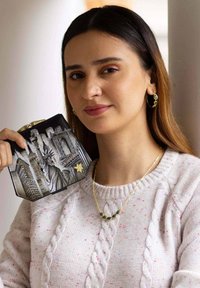 Zwarte, gestructureerde clutch met een zilveren ontwerp van het Vrijheidsbeeld en de stadsgezichten; model draagt een crèmekleurige trui met een kabelbrei patroon.