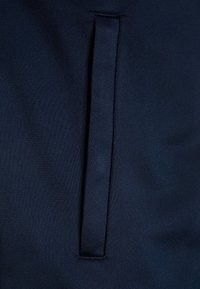 Navy blue fabric featuring a textured weave, with a prominent vertical seam and a sleek, integrated pocket detail.