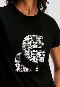 Black t-shirt featuring a white sequin appliqué of a stylized profile with sunglasses, outlined in black stitching. Short sleeves.