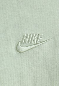 Logo Nike vyšitý bílou nití na světle zeleném textilním pozadí.