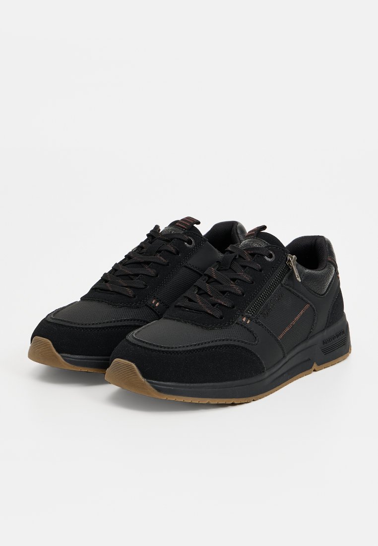 Chaussures de sport noires présentant une combinaison de matériaux lisses et texturés, avec un laçage à l'avant et une semelle en caoutchouc marron contrastante.