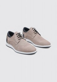 Zapatos de vestir beige con cordones, que cuentan con una parte superior texturizada perforada y detalles en azul marino, con una suela blanca y cordones negros.