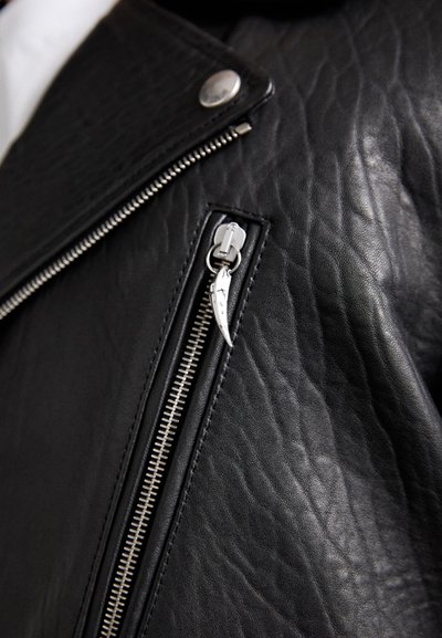 Black leather jacket with a textured finish, featuring a silver zipper detail and hardware, as well as a diagonal pocket zipper.