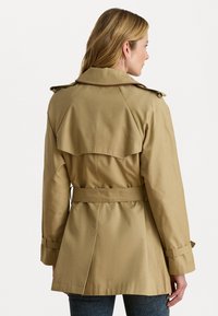 Manteau trench kaki avec une taille ceinturée, des épaulettes et une fente au dos. Le design présente un col classique et des manches longues.