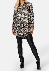 Beige zebra print shirt dress with button closure, long sleeves, and high-low hem, paired with fitted black leather pants and ankle boots.
