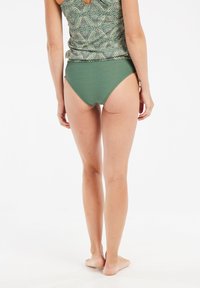 Žalias raštuotas tankinis viršus su apvaliu nugaros kirpimu, derinamas su vientisais žaliais aukšto liemens bikini apatiniais, turinčiais tekstūruotą geometrinį raštą.