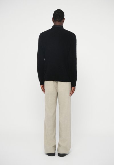 Maglione nero e peloso con colletto alto, abbinato a pantaloni beige chiaro e morbidi. La texture sembra morbida, con un design dalla vestibilità rilassata.