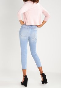 Ljusrosa kortärmad tröja i figursydd stil, i kombination med ljusblå högmidjade jeans. Svarta högklackade skor avslutar outfiten.